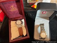 Both watches displayed in their cases; Catamaran with brown leather band and Swiss Army with metal band
