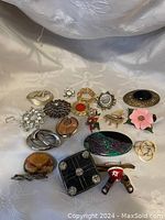 Full collection of 18 vintage brooches arranged on a cloth background, showcasing variety in shape, color and design.