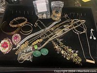 Overview of assorted fashion jewelry pieces including bracelets, necklaces, brooches, and earrings in a black display tray.