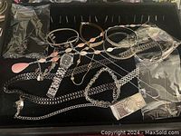 Collection of assorted silver-tone fashion jewelry including chain bracelets, necklaces, and wristwatch with rectangular face.