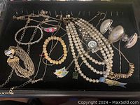 Full display of assorted fashion jewelry including Monet bracelet, pearl necklaces, and various bracelets/pendants.