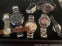 Overview of seven assorted brand wristwatches in tray, showing mixed metal and leather straps, various dial designs.