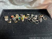 Photo showing the full set of 34 assorted fashion rings laid out on a black display tray, various colors and styles visible