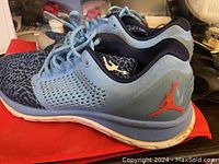 Side view of Nike Jordan athletic shoe in blue and black with orange logo, showing condition of sole and upper.