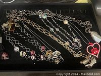Top view of assorted metal chain necklaces featuring various clear and amber faceted glass crystals along with a red crown rhinestone pendant on black display tray.