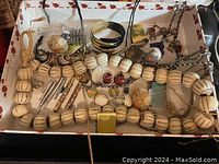 Top-down view of a white box filled with assorted jewelry items such as bead necklaces, bracelets, brooches, earrings, and miniature vintage pens and pencils.