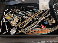 Overview photo showing the assortment of fashion jewelry including necklaces, bracelets, earrings, and pendants laid out in a black tray.