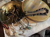 Metal tin filled with various necklaces and fashion jewelry with a patina on the tin lid.