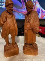 Photo showing both hand carved wooden figurines of a man and woman on bases, verifying detail and condition