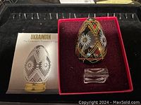 Vintage Ukrainian decorated egg with floral and geometric patterns, displayed in an open red velvet-lined box with missing top cover and a small clear stand.