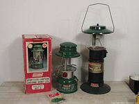 Two Coleman camping lanterns, one with original box and accessories beside it