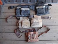 All three tool belts laid out on wooden floor, showing two canvas Klein Tools belts and one leather Kunys belt
