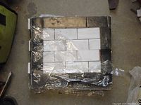 Four white brick mosaic tiles wrapped in plastic on a wooden pallet.