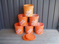 Six orange plastic buckets stacked in a pyramid formation, showing The Home Depot logo on the front. Two lids placed in front of buckets.