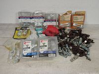 Lot of cabinet hardware and hinges including metal cabinet hinges, packs of Richelieu cabinet knobs in brushed nickel, closet door guides, a red strap, and various screws.