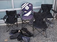 Four folding camping chairs displayed outside on gravel in front of glass window. Purple Toronto Maple Leafs chair in center, three black chairs around it, two black carrying bags on the ground.