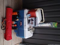 Full view of camping items including coolers, rolled red hammock, water bottles, camping mug and accessories.