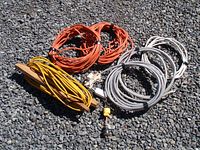 Lot showing all extension cords and cords with metal conduit arranged on gravel surface.