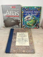 Photo showing all three books standing upright: The Canadian Atlas, Children's Atlas of the World, The Wall Chart of World History.