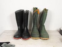 Pair of black rubber boots and green insulated rubber boots standing side by side on a wooden surface against white background.