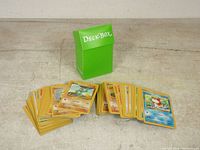 Overall lot of loose Pokemon cards with green Deck Box in the background, cards spread in three piles showing varying characters and types.