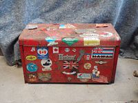 Front view of the red metal Herbrand toolbox covered with vintage stickers and a central metal logo plate.
