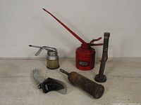 Photo of five vintage oil-related tools including red Wesco oil can, small oil can, grease gun tool, tall oil spout, and flexible spout tool.
