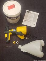 Main sprayer gun, detachable hopper, nozzle parts, power cord, user manual, and full paint bucket laid out on dark surface