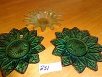 Three decorative small glass dishes on a wooden surface: two green leaf-shaped and one amber sunburst-shaped.