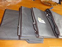Four folded grey fabric storage bags with brown edging laid out on a wooden surface, showing the fabric texture and folds.
