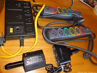 Lot overview showing two multi-outlet power strips with colored outlets, a black Woods power strip and black power supply adapter unit.