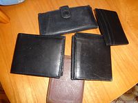 Five leather card cases and wallets arranged on wooden surface, showing variety of shapes and colors including black and tan