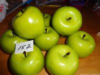 Photo showing eight imitation Granny Smith apples arranged on wooden surface, highlighting their bright green color and brown stems.