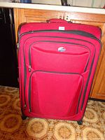 Front view of large red suitcase upright showing multiple zippered pockets, American Tourister logo, and overall clean condition with minor marks.