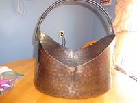 Front angle view of large hammered metal basket-style container with handle set on wooden table.