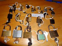 Overview of more than 15 locks of various brands and sizes laid out on a wooden surface with keys tied by white strings