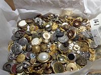 Broad view of a large collection of mixed metal buttons in gold, silver, and brass tones with various decorations, including pearl-like centers.