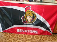 Front side of large Ottawa Senators flag showing full team logo and 'SENATORS' text on floor background.