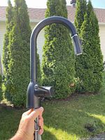 Front view of the black matte pull down kitchen faucet held outdoors showing the high curved neck and integrated spray head.