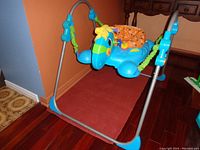 Front view of blue rocking horse toy on metal frame with orange seat and green fabric support straps