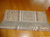 Folded table runner showing beige and taupe geometric pattern and fringe end detail