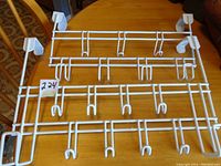 Two white metal over-the-door hangers displayed on a wooden table, showing their size and hook arrangement.