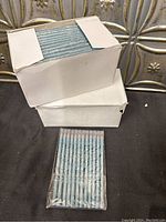 Two white boxes stacked containing multiple blue eyeliner pencils inside, one box top open showing packaged pencils inside.