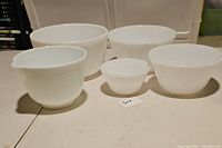 Five white glass mixing bowls arranged on table showing two sets; Hamilton Beach with a spout and Federal Glass without