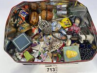 Top-down view of the tin filled with assorted small collectibles including thimbles, smaller figurines, pins, and other items.