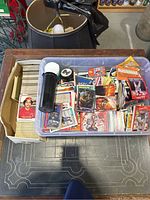 Photo of a plastic storage bin containing a variety of sports and comic cards, including baseball and football.