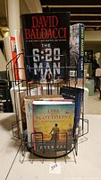 Front view of the metal swivel rack holding books including The 6:20 Man by David Baldacci and Eternal by Lisa Scottoline.