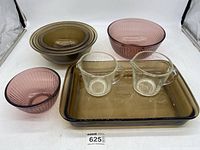 Full lot showing three amber Pyrex Visions mixing bowls, one amber casserole dish, two clear glass measuring cups, and two pinkish-red glass bowls.