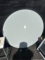 Top view of the round white/light gray table top with a diameter of approximately 48 inches, showing smooth surface with a label.
