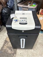 Front view of shredder showing rectangular waste bin with clear strip, top white panel with control buttons and key lock.